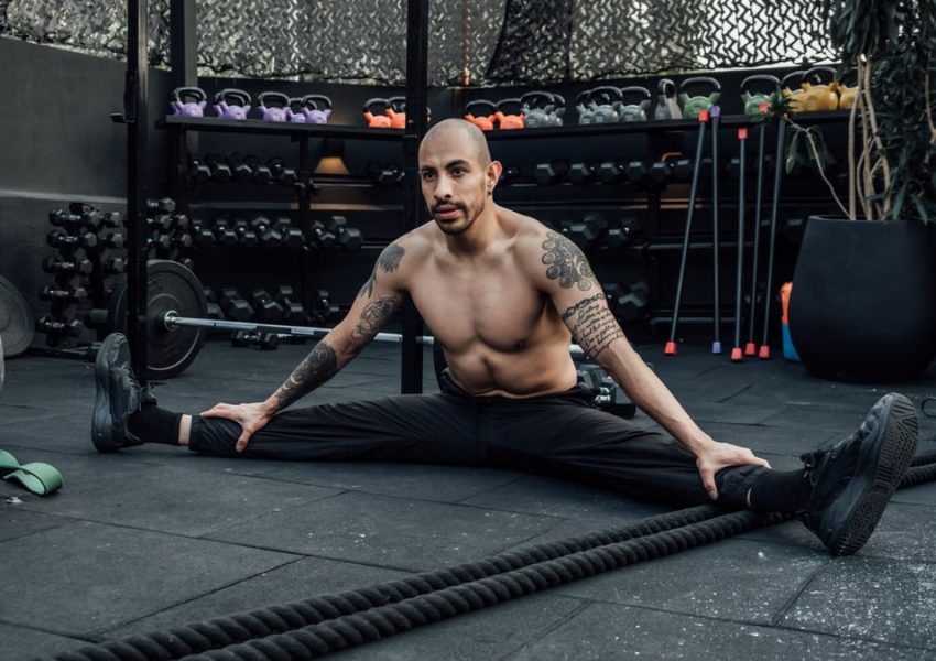 Tattooed man performing a split stretch in a gym, showcasing flexibility and fitness lifestyle in Mexico City.